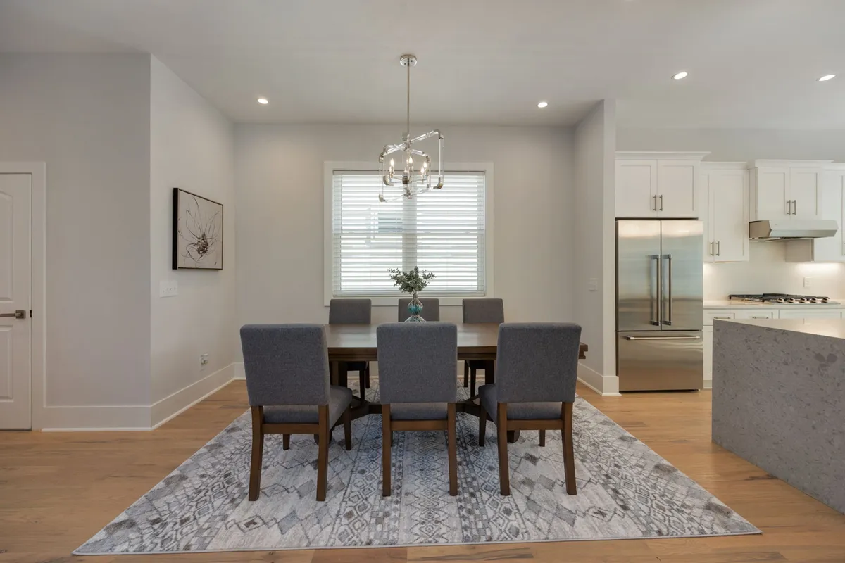 This interior shot features a dining table set for six, bathed in natural light from surrounding windows and illuminated by a chandelier overhead. A patterned rug and cozy decor complete the welcoming dining space, perfect for group meals and shared moments.