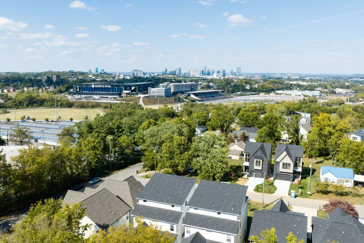 A panoramic view of the Nashville city skyline featuring a sports stadium, green trees, and residential rooftops, all under an energetic, lively atmosphere. The view captures the vibrancy of city life and the proximity to Nashville’s urban attractions.