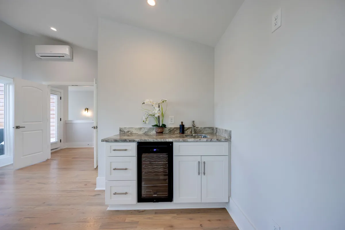 A sleek wet bar area featuring a countertop, wine cooler, sink, and a floral arrangement, exuding sophistication and readiness for entertaining. This intimate setting is ideal for sharing drinks and planning an evening out or enjoying quiet conversation.