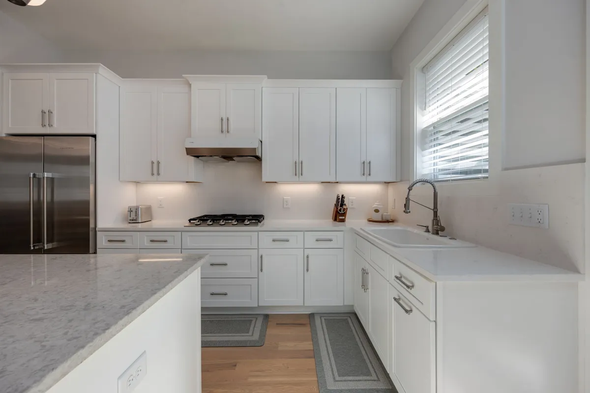 This image features a modern kitchen with stainless steel appliances, including a refrigerator and gas stove, white cabinetry, and a sleek sink with faucet. The space is bright, inviting, and clean, reflecting a chef-inspired atmosphere ideal for group cooking and family meals.
