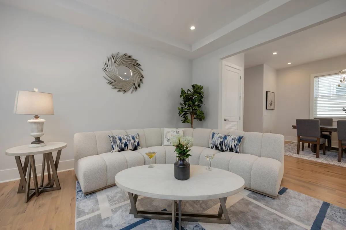 A chic, cozy living room featuring a curved sectional sofa, round coffee table, decorative mirror, potted plant, and a table lamp. The open and inviting layout encourages group conversations and intimate gatherings, perfectly capturing the essence of a modern social hub.