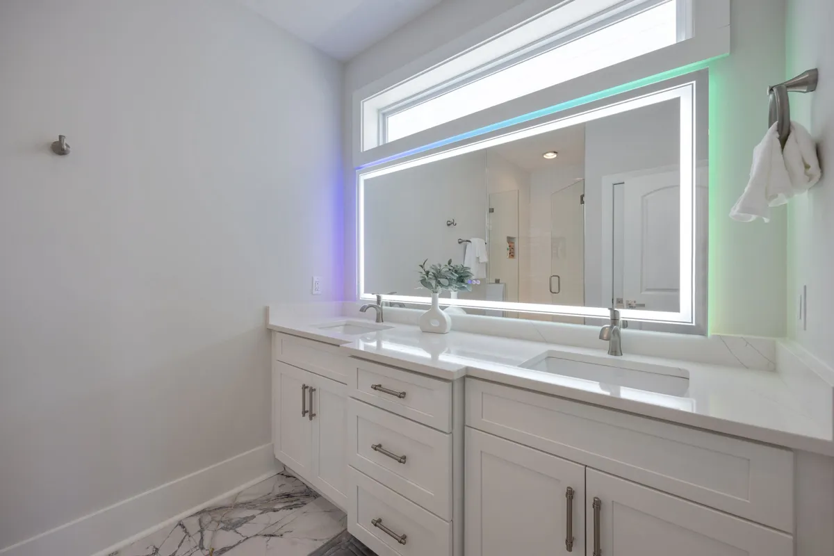 A modern bathroom with dual sinks, an illuminated mirror, and marble flooring, offering a clean and serene setting for self-care and morning routines.