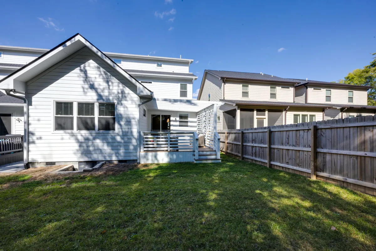 A view of a white house exterior showcasing a lush, fenced grass backyard and a connecting deck area. The space feels inviting and safe, with plenty of room for children or pets to play, making it ideal for families.