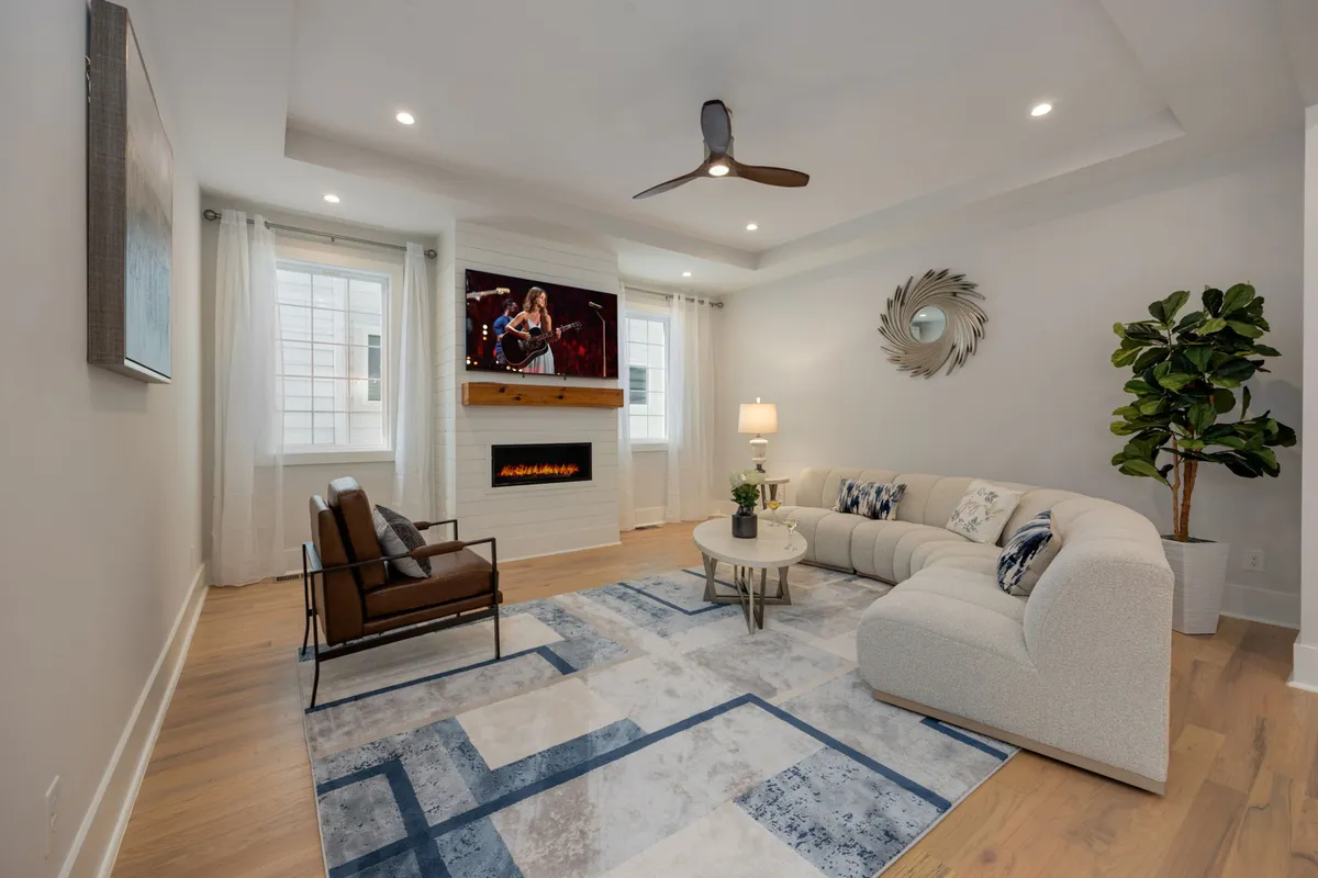 A spacious living area with a large sectional sofa, modern coffee table, electric fireplace, TV displaying performance art, and an indoor plant. The arrangement is ideal for gatherings, game nights, or relaxed family time with a luxe-meets-comfort vibe.